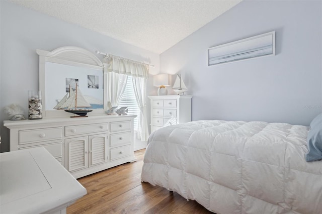 bedroom with vaulted ceiling, hardwood / wood-style floors, and a textured ceiling