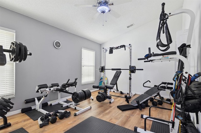 exercise area with ceiling fan, hardwood / wood-style flooring, vaulted ceiling, and a textured ceiling