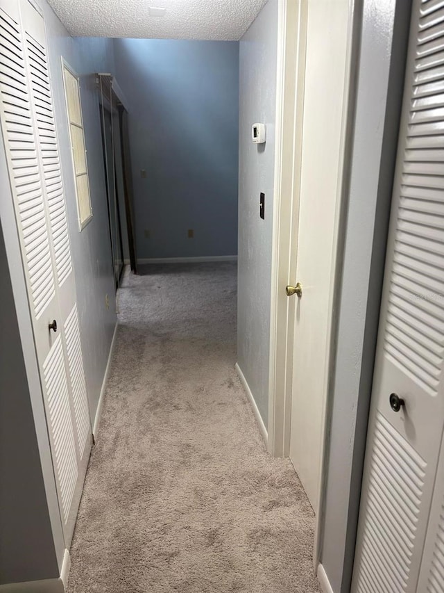 corridor with light colored carpet and a textured ceiling