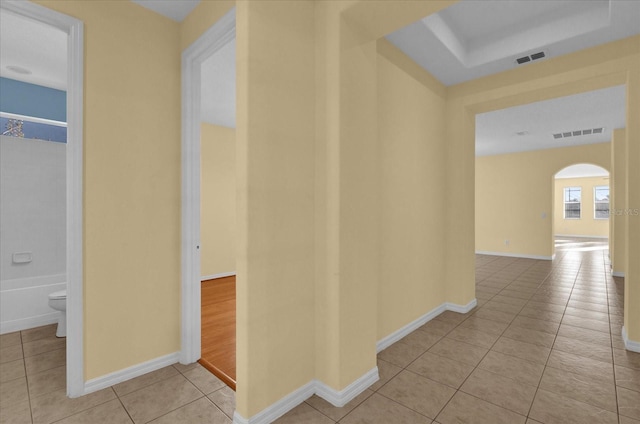 hallway featuring light tile patterned floors and a tray ceiling