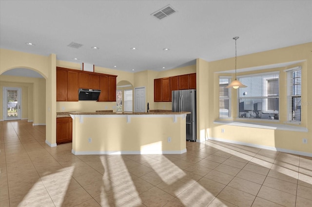 kitchen featuring pendant lighting, ventilation hood, stainless steel fridge, light tile patterned floors, and an island with sink