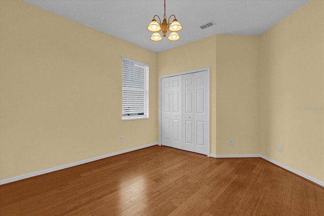 unfurnished bedroom featuring wood-type flooring, an inviting chandelier, and a closet