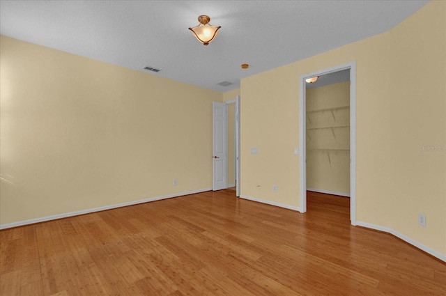 unfurnished bedroom with a spacious closet, a closet, and hardwood / wood-style flooring