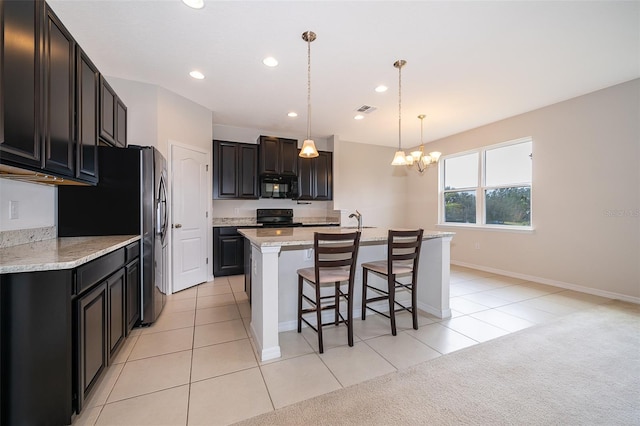 kitchen featuring light carpet, light stone counters, black appliances, a center island with sink, and hanging light fixtures