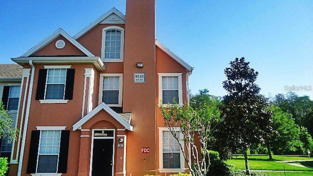 view of property with a front yard, a chimney, and stucco siding