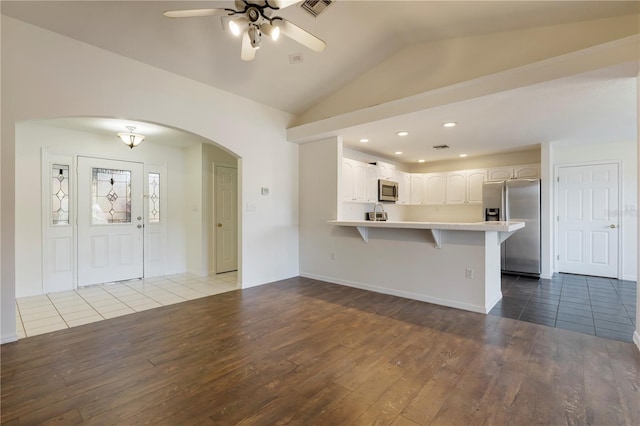 kitchen with white cabinetry, kitchen peninsula, lofted ceiling, a breakfast bar, and appliances with stainless steel finishes