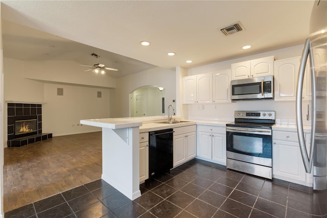 kitchen with kitchen peninsula, white cabinetry, a tiled fireplace, and appliances with stainless steel finishes