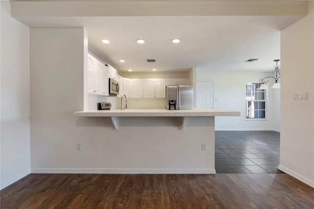 kitchen with a breakfast bar, tile counters, kitchen peninsula, stainless steel appliances, and white cabinets