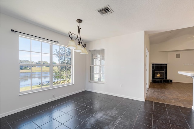 unfurnished dining area with a tiled fireplace, dark tile patterned flooring, a textured ceiling, and a water view