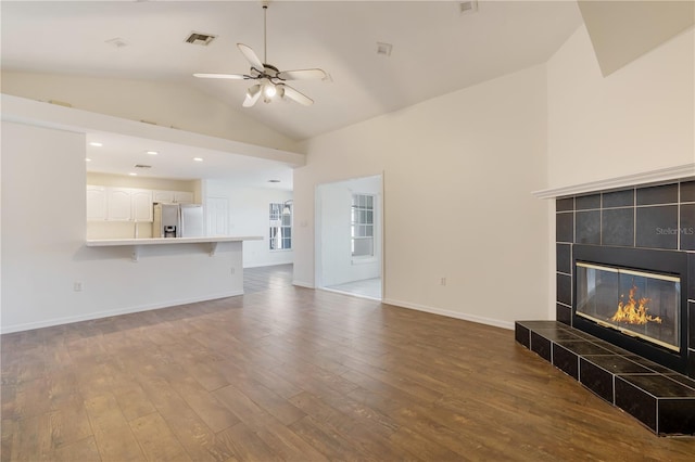 unfurnished living room with lofted ceiling, wood-type flooring, a tile fireplace, and ceiling fan