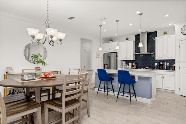 kitchen with white cabinetry, wall chimney range hood, decorative light fixtures, and stainless steel fridge