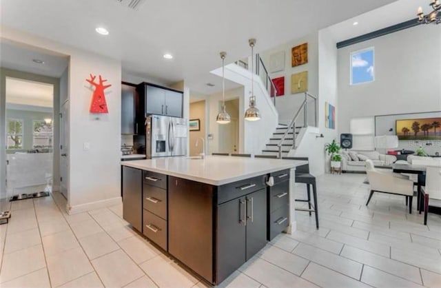 kitchen featuring stainless steel fridge, decorative light fixtures, a breakfast bar area, a kitchen island with sink, and light tile patterned floors