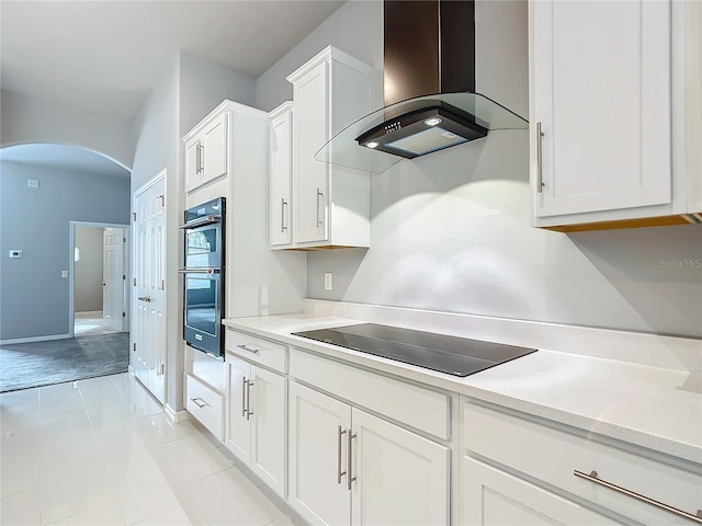 kitchen featuring white cabinets, island range hood, light tile patterned flooring, and black appliances