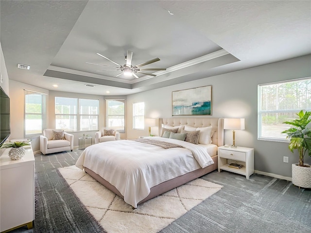 carpeted bedroom featuring a tray ceiling, multiple windows, and ceiling fan