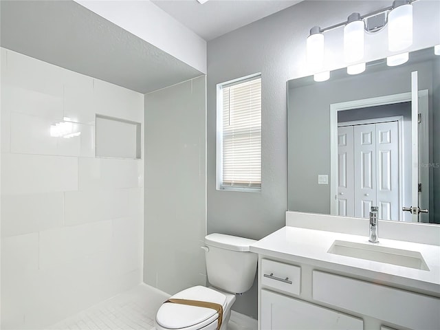 bathroom with plenty of natural light, toilet, a tile shower, and vanity