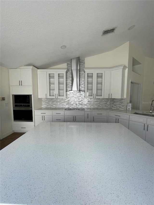 kitchen with vaulted ceiling, backsplash, wall chimney range hood, and stainless steel oven