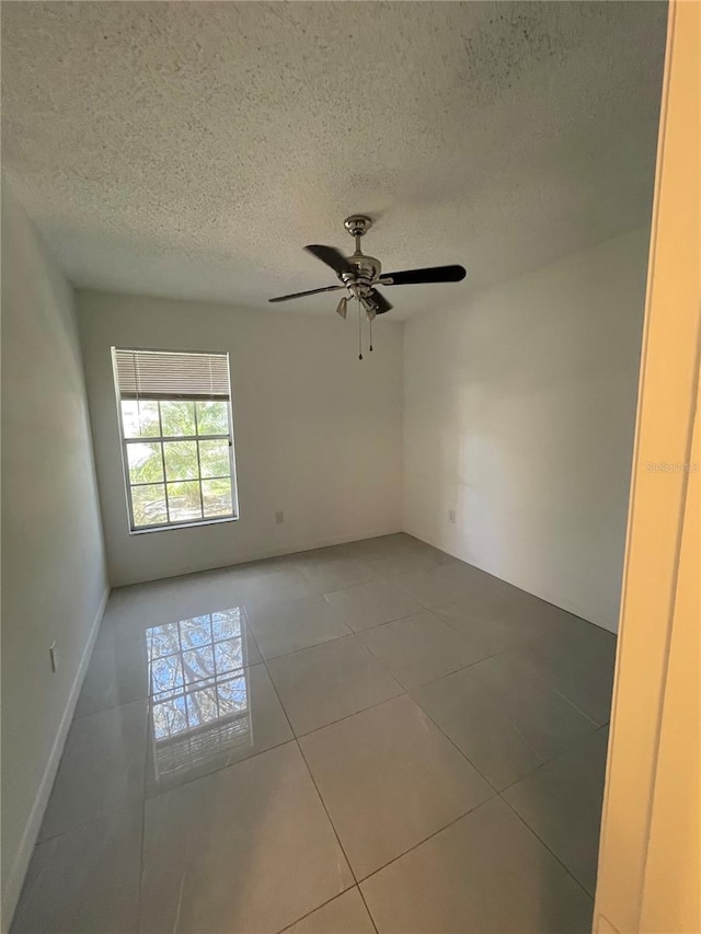 empty room with tile patterned floors, a textured ceiling, and a ceiling fan