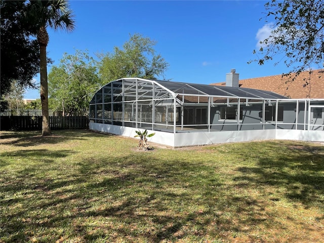 back of property with glass enclosure, a chimney, a yard, and fence