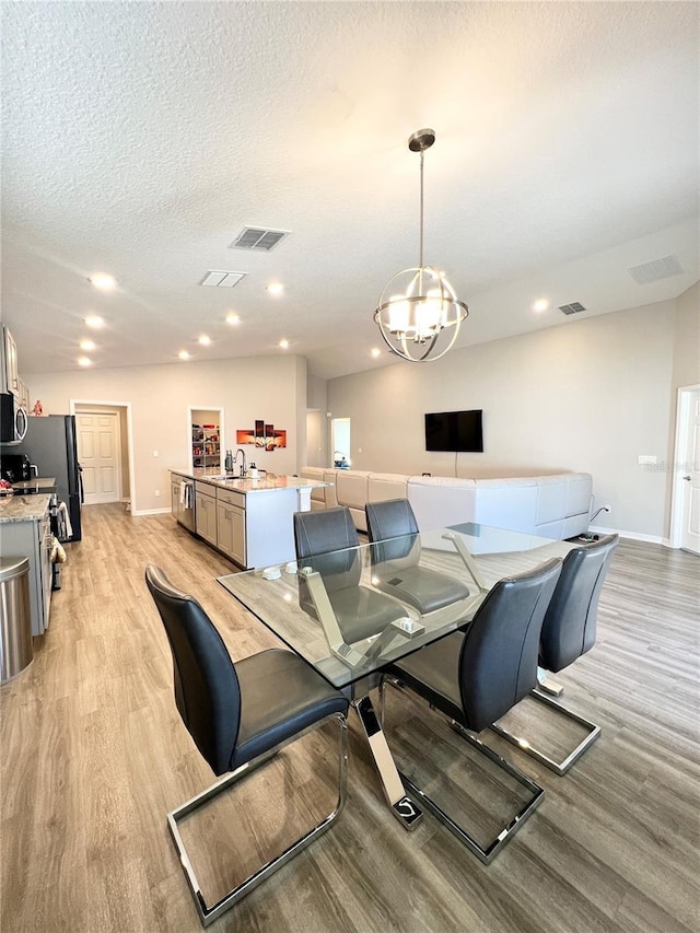 dining space with sink, light hardwood / wood-style floors, a textured ceiling, and an inviting chandelier