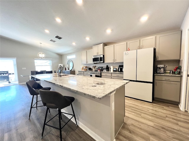 kitchen featuring a kitchen bar, decorative backsplash, stainless steel appliances, a kitchen island with sink, and lofted ceiling