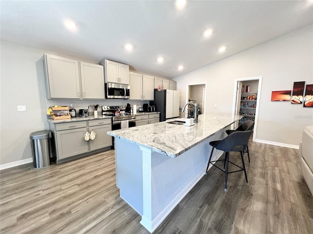 kitchen featuring gray cabinetry, a center island with sink, sink, appliances with stainless steel finishes, and a kitchen bar