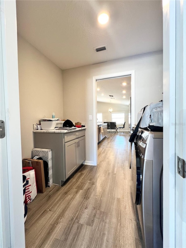 laundry area featuring washing machine and clothes dryer, cabinets, a textured ceiling, and light wood-type flooring