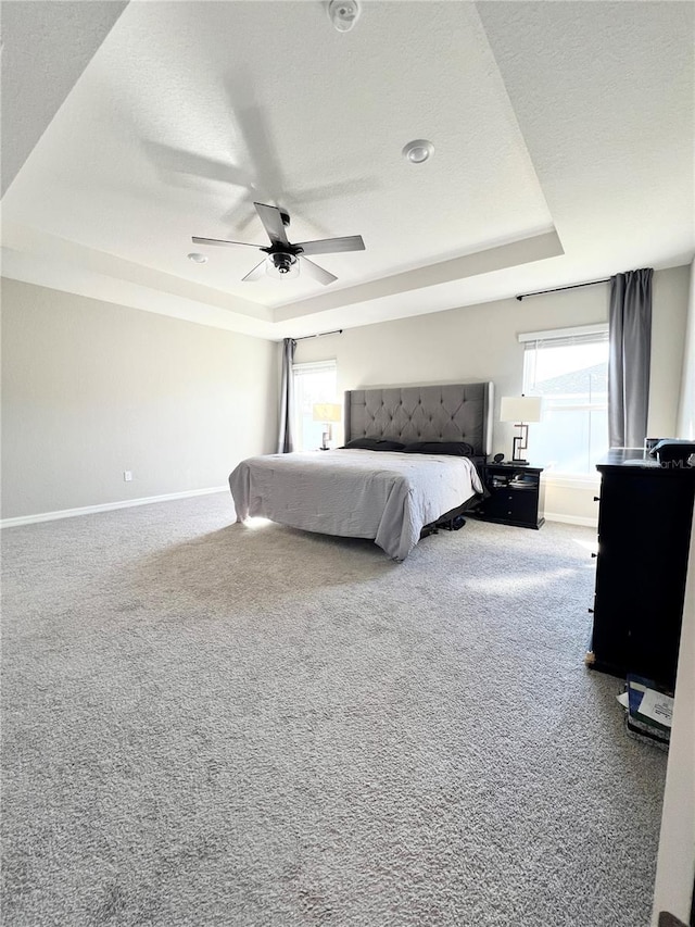 carpeted bedroom with a textured ceiling, ceiling fan, multiple windows, and a tray ceiling