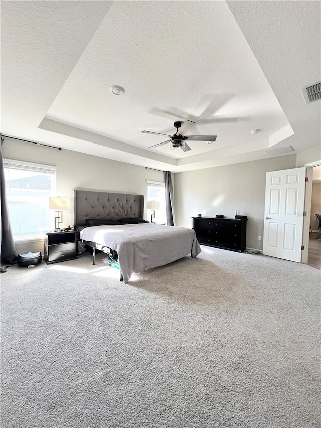 carpeted bedroom with ceiling fan, a raised ceiling, and a textured ceiling