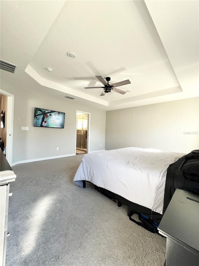 bedroom featuring a raised ceiling, ceiling fan, and ensuite bathroom