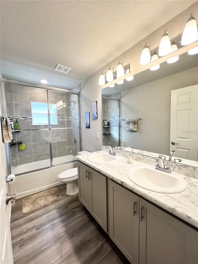 full bathroom featuring bath / shower combo with glass door, vanity, wood-type flooring, and a textured ceiling