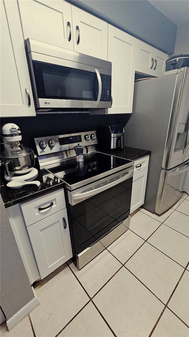 kitchen featuring stainless steel appliances, white cabinetry, dark stone counters, and light tile patterned flooring