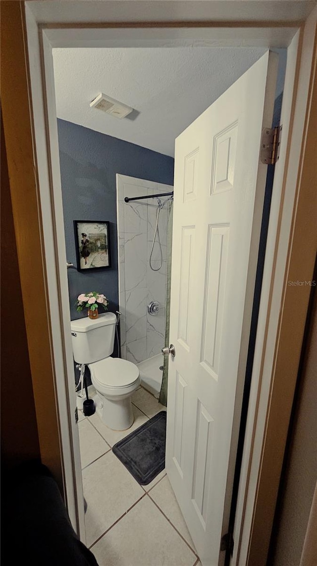 bathroom with toilet, a tile shower, and tile patterned floors