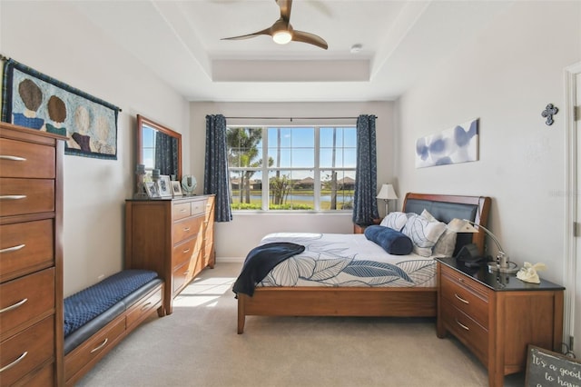 bedroom with ceiling fan, light carpet, and a tray ceiling