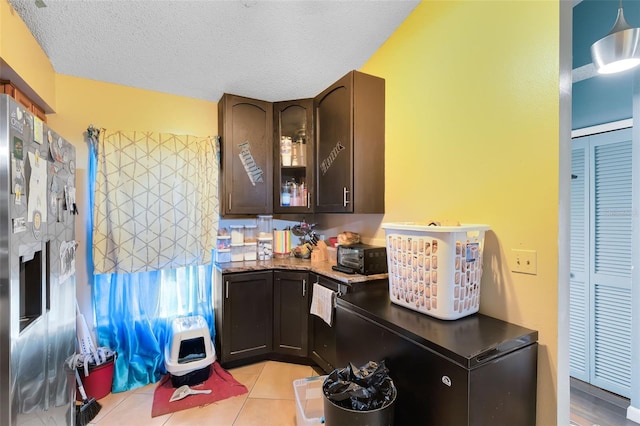 kitchen featuring light tile patterned floors, refrigerator, a textured ceiling, and dark brown cabinets