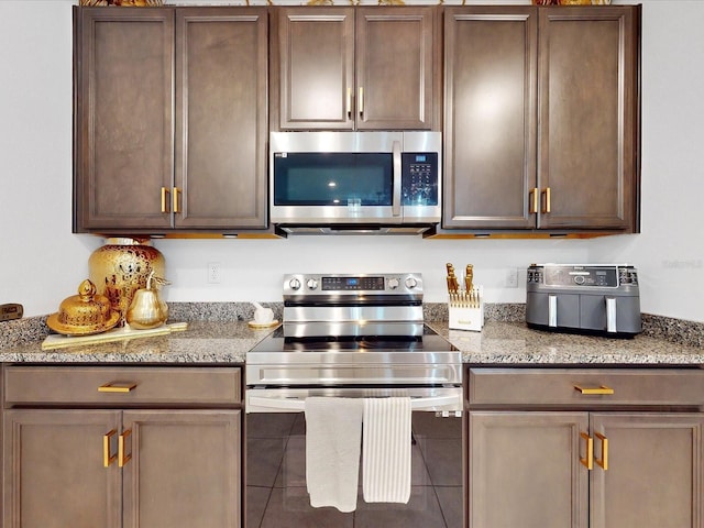 kitchen featuring tile patterned flooring, dark brown cabinetry, stainless steel appliances, and stone counters