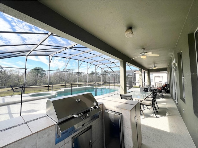 view of patio featuring ceiling fan, glass enclosure, exterior kitchen, and an outdoor pool