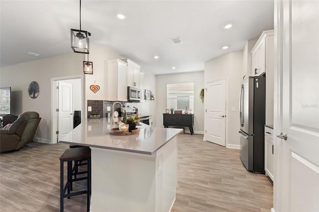 kitchen with pendant lighting, white cabinetry, stainless steel appliances, tasteful backsplash, and a breakfast bar area