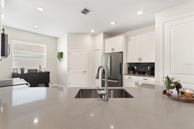 kitchen featuring white cabinets, stainless steel fridge, backsplash, and sink