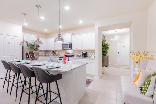 kitchen featuring a kitchen bar, white cabinets, hanging light fixtures, and appliances with stainless steel finishes