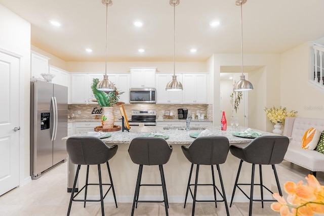 kitchen with pendant lighting, stainless steel appliances, white cabinetry, and an island with sink