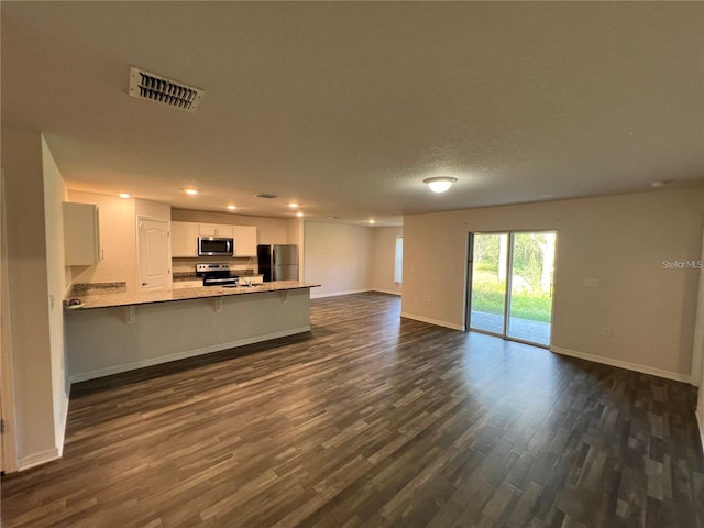 interior space featuring kitchen peninsula, appliances with stainless steel finishes, a breakfast bar, white cabinets, and dark hardwood / wood-style floors