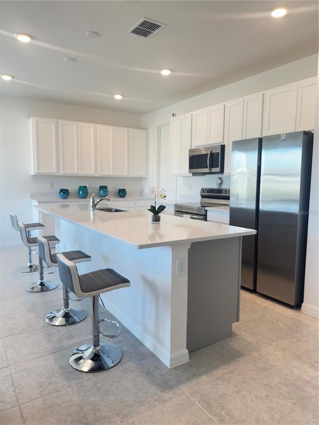 kitchen featuring a kitchen bar, appliances with stainless steel finishes, sink, white cabinets, and an island with sink