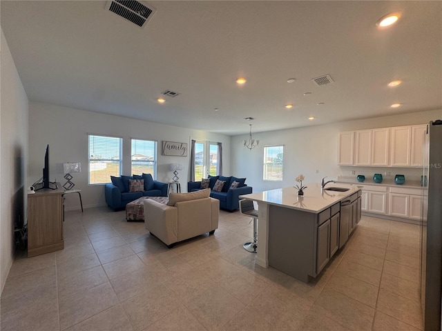 kitchen featuring sink, light tile patterned floors, a notable chandelier, a center island with sink, and white cabinets