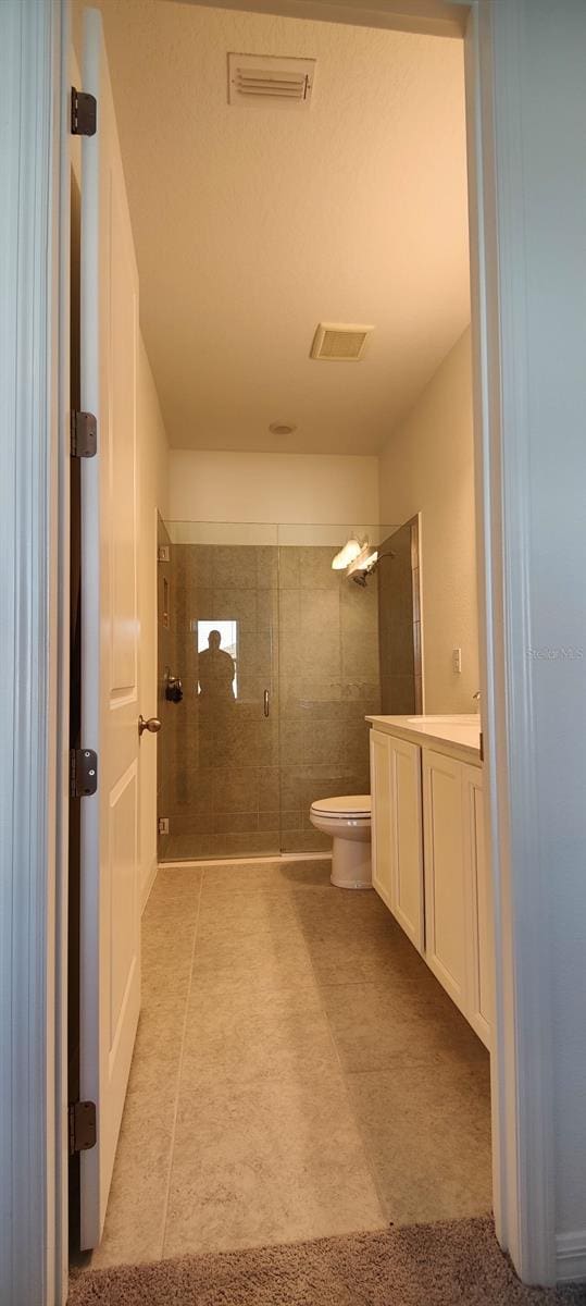 bathroom featuring tile patterned flooring, vanity, toilet, and a shower with door