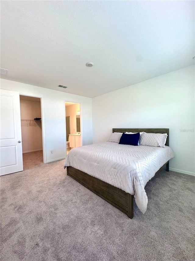 bedroom with light carpet, a closet, ensuite bath, and a spacious closet