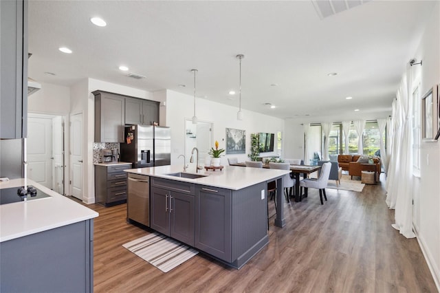 kitchen with stainless steel appliances, a kitchen island with sink, sink, gray cabinets, and hanging light fixtures