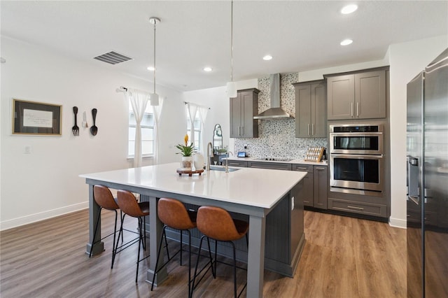 kitchen with sink, hanging light fixtures, wall chimney range hood, a kitchen breakfast bar, and an island with sink