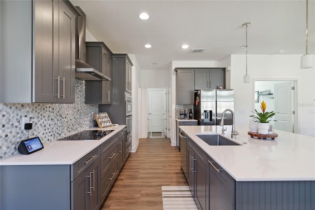 kitchen featuring wall chimney range hood, sink, hanging light fixtures, black electric cooktop, and stainless steel fridge with ice dispenser