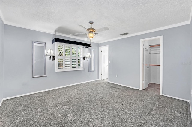 unfurnished bedroom with a walk in closet, a textured ceiling, ceiling fan, crown molding, and a closet