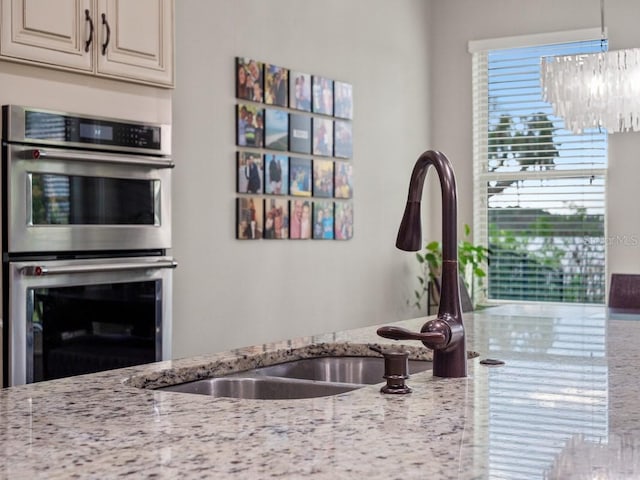 kitchen featuring light stone countertops, stainless steel double oven, sink, a chandelier, and white cabinetry